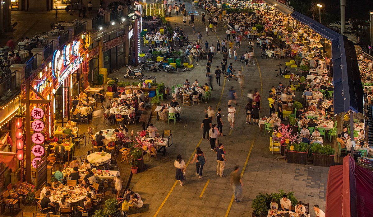 湘江大碼頭前坪裏，有序擺放的露天餐桌上坐滿了市民和遊客、與前來納涼的的路人交織，就像置身鬧市街區。